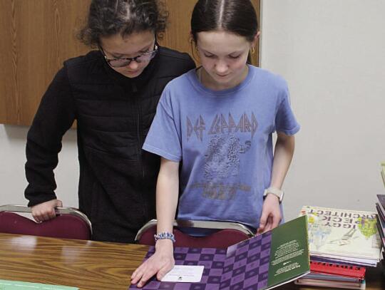Above, Elliot and Evynn Kumm hold two of the 114 books donated to the Osmond Public Library because of a donation by the Kumm family and the Pilcrow Foundation. Below, Evynn places a book plate in one of the books donated to the library.