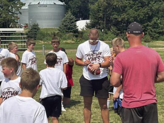 In top photo, the group of youth attending the camp poses with Christian Jones and Cornhusker football players. Bottom left: Jones gives instructions to group of young athletes. Bottom right: Jones autographs football for one of the football camp attendee